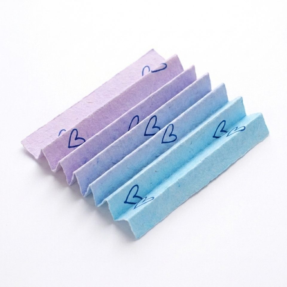 A lavender and blue heart-decorated paper rectangle folded into an accordion fan.