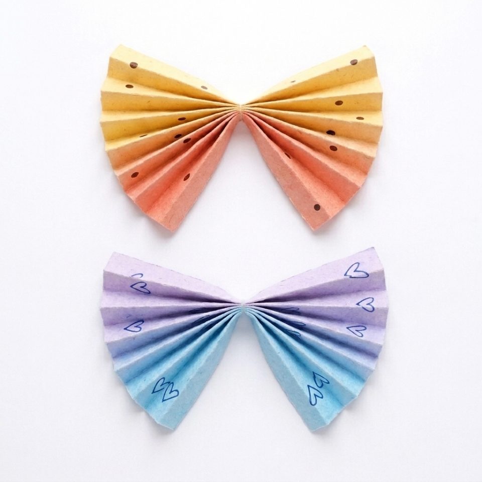 Two colorful accordion paper fans pinched in the middle to make upper and lower wing pairs.