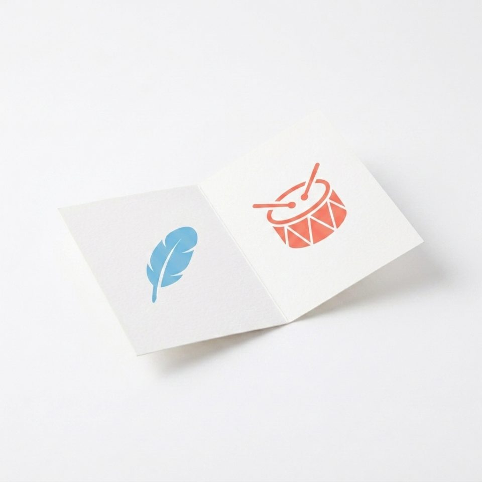 A folded white paper volume card with a blue feather symbol and a coral drum symbol.