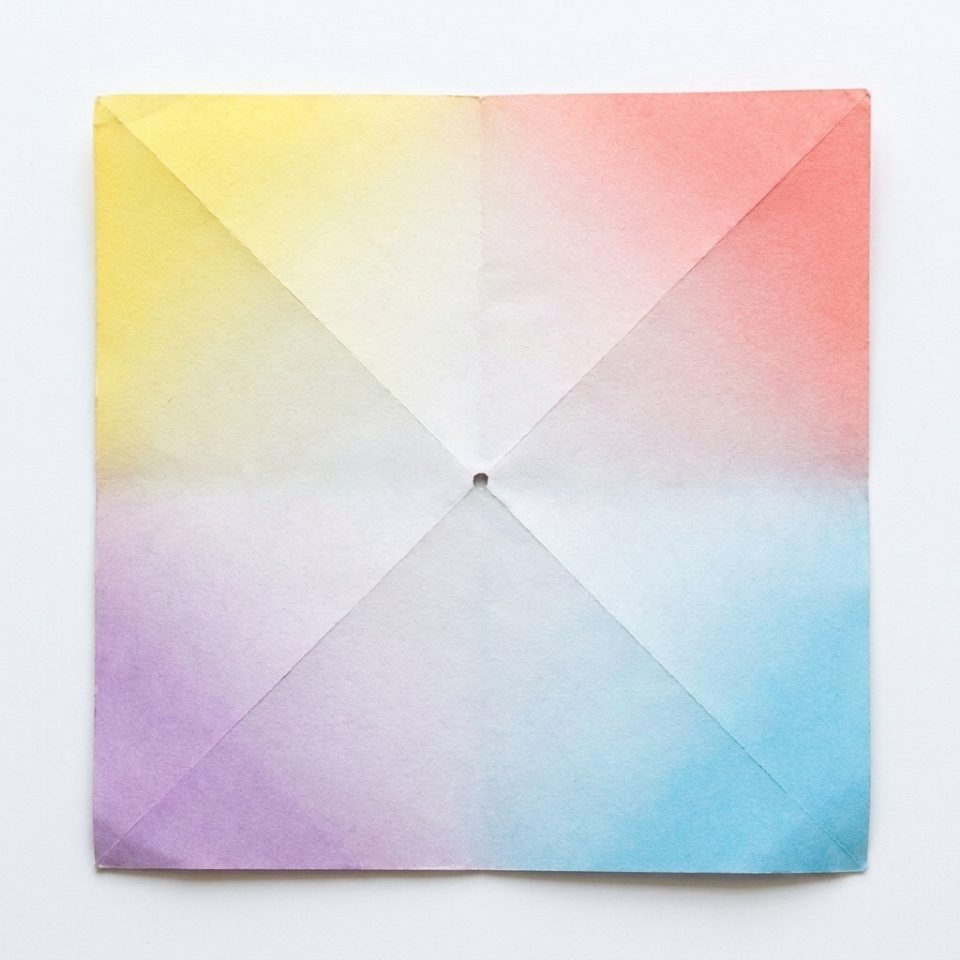 A colored paper square with diagonal folds and a small hole in its center.