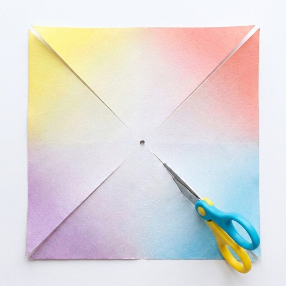 A colored paper square with four diagonal cuts that stop before the center hole.