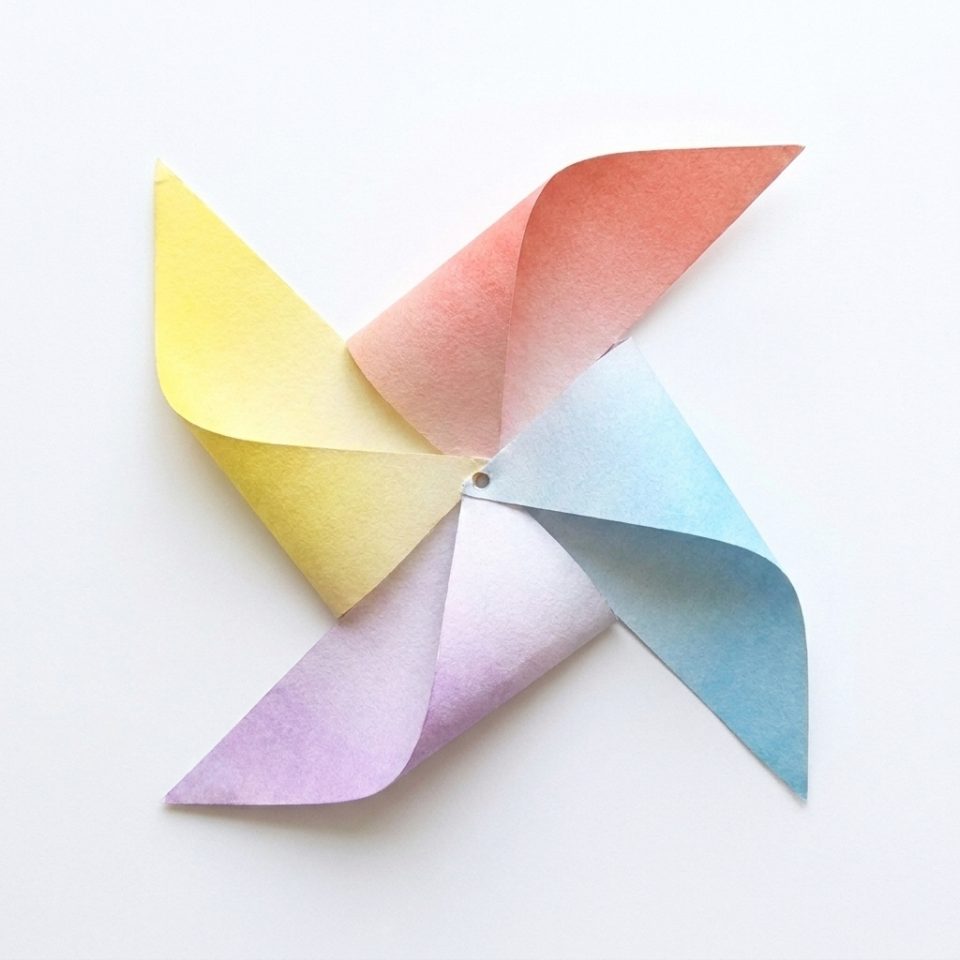 A colorful paper pinwheel with its four folded blades meeting at the center.