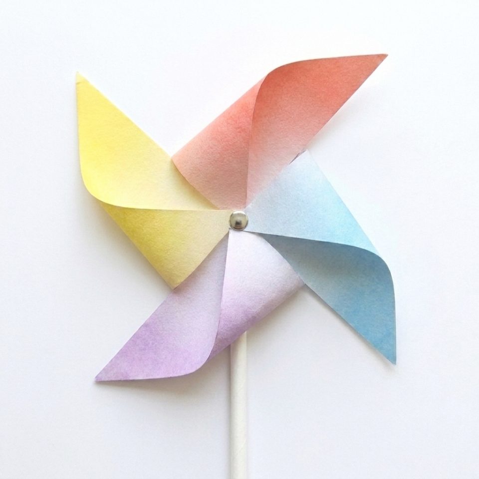 A finished colorful paper pinwheel attached to a white paper straw with a round center fastener.